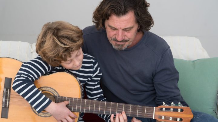 Un père apprend à jouer de la guitare à son fils dans un salon.